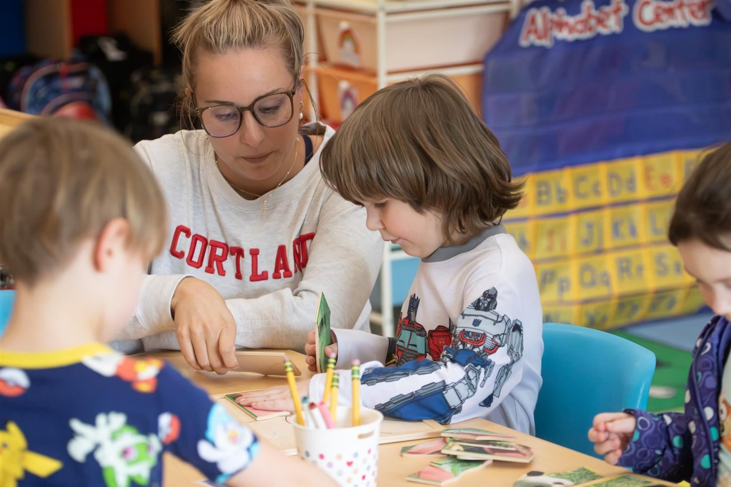 Students play at a table with their teacher